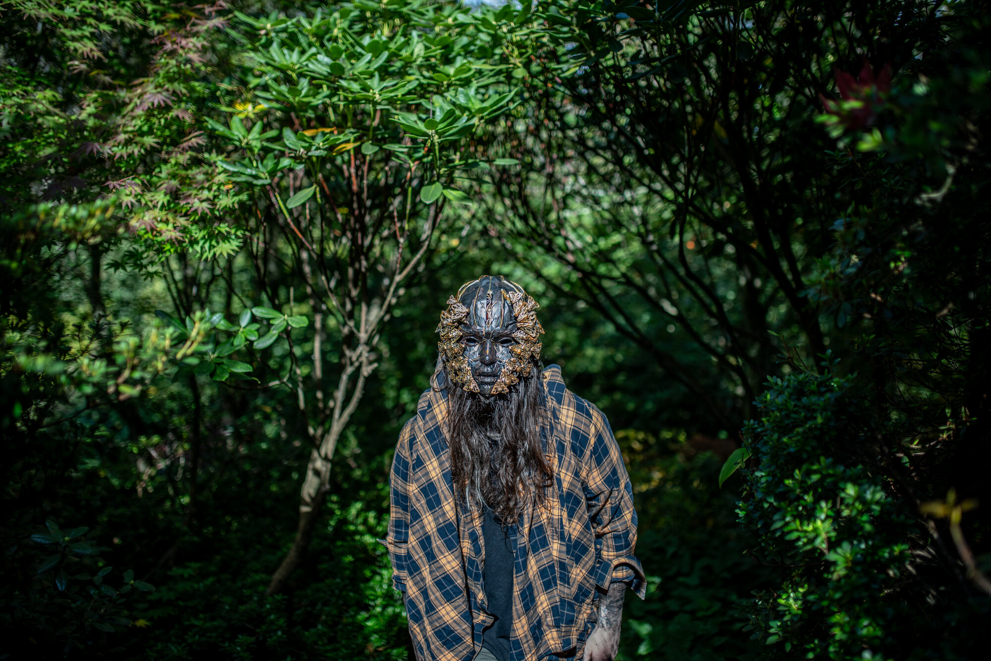 Wearable mask, dark carved face with butterfly crown, forest tunnel