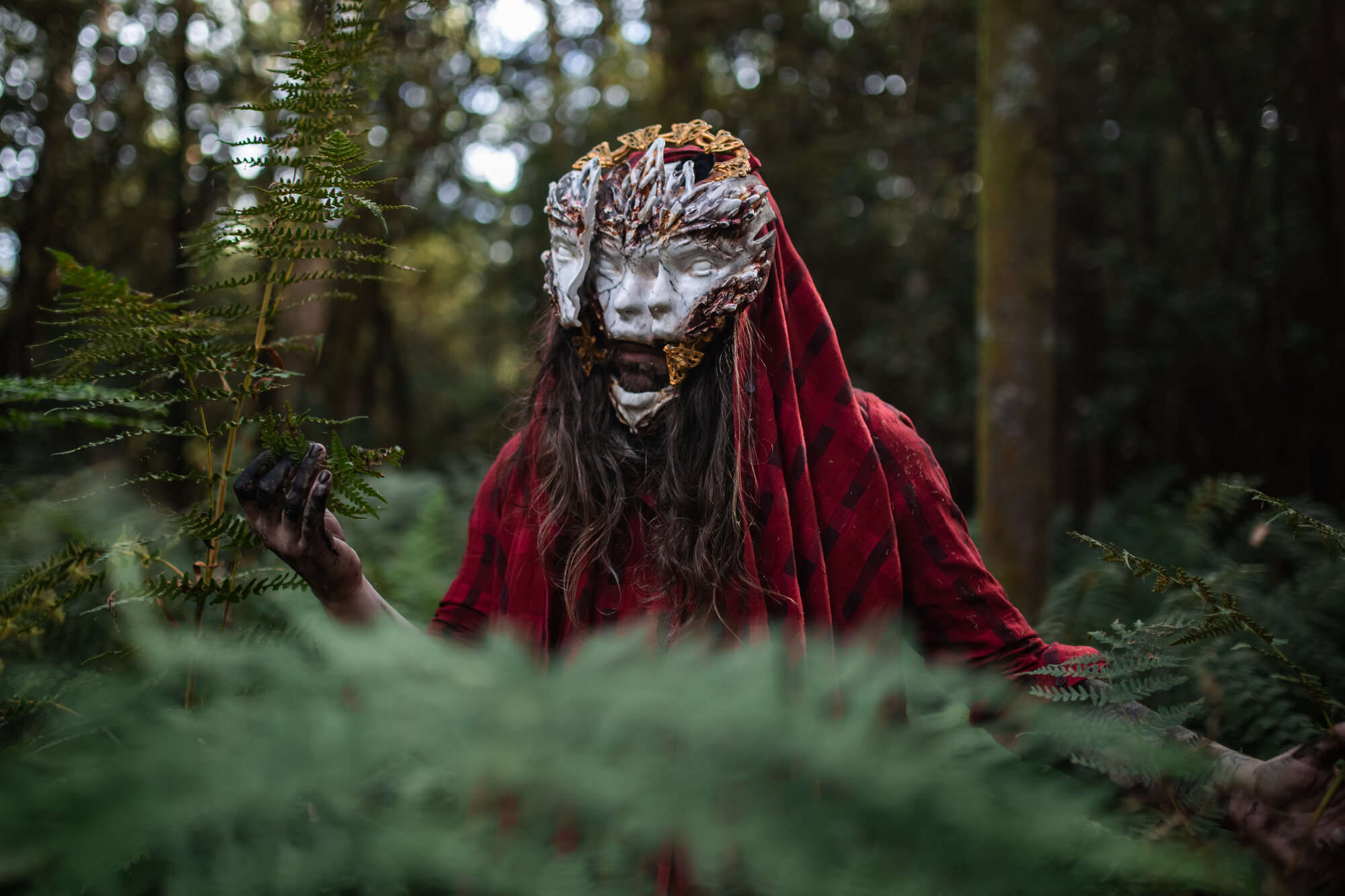 Wearable mask, twin carved faces with gold crown, forest setting